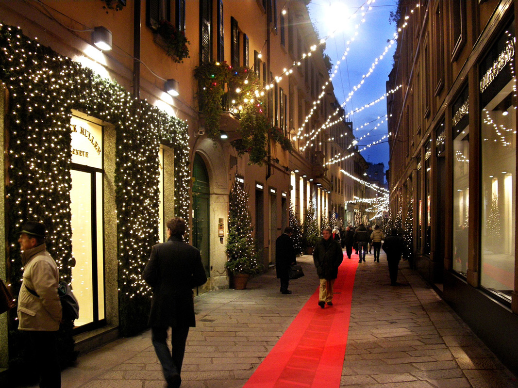Milan shopping street decked with string lights and a red carpet at dusk
