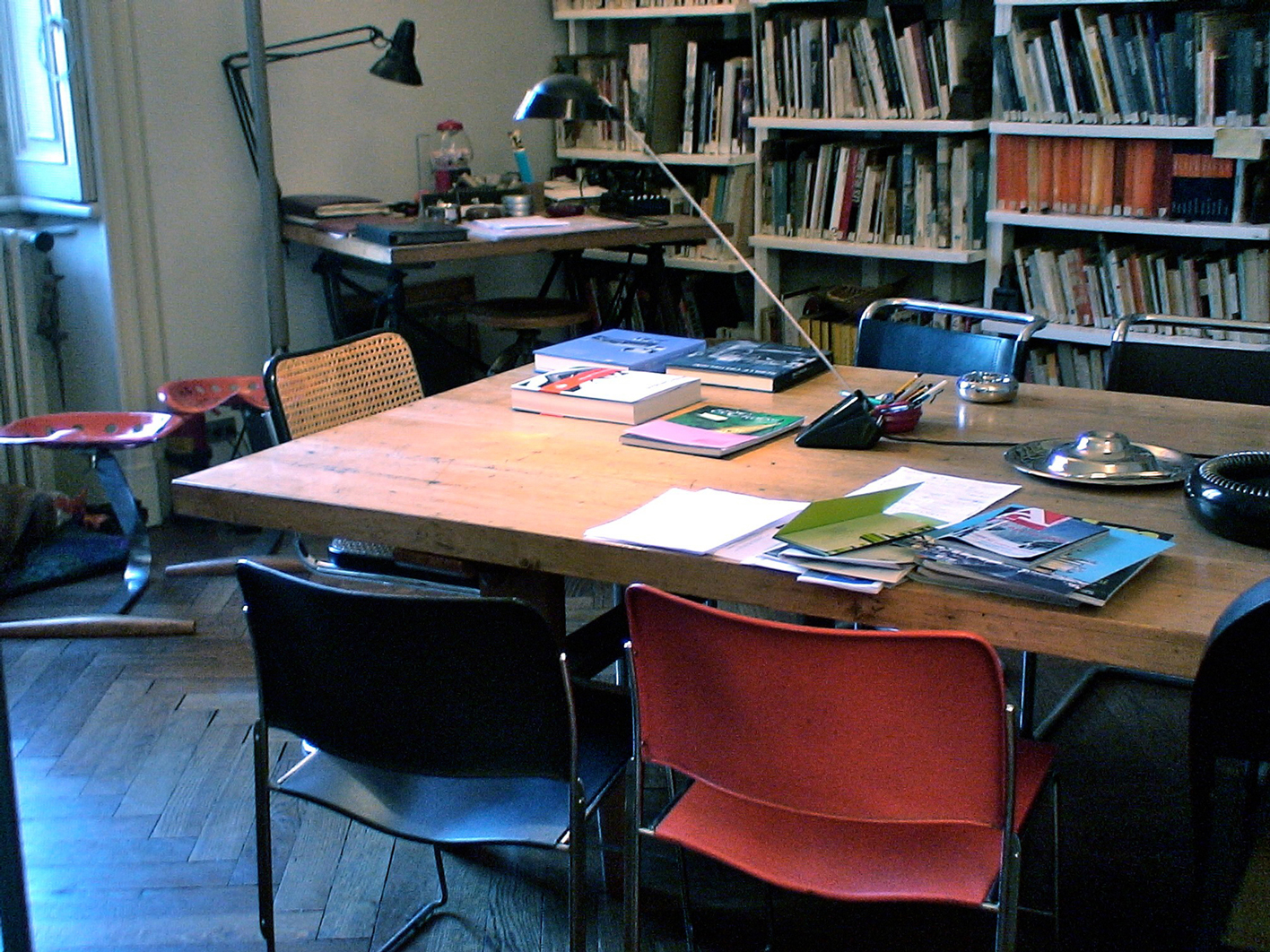 Wooden library table surrounded by chairs with bookshelves in the background