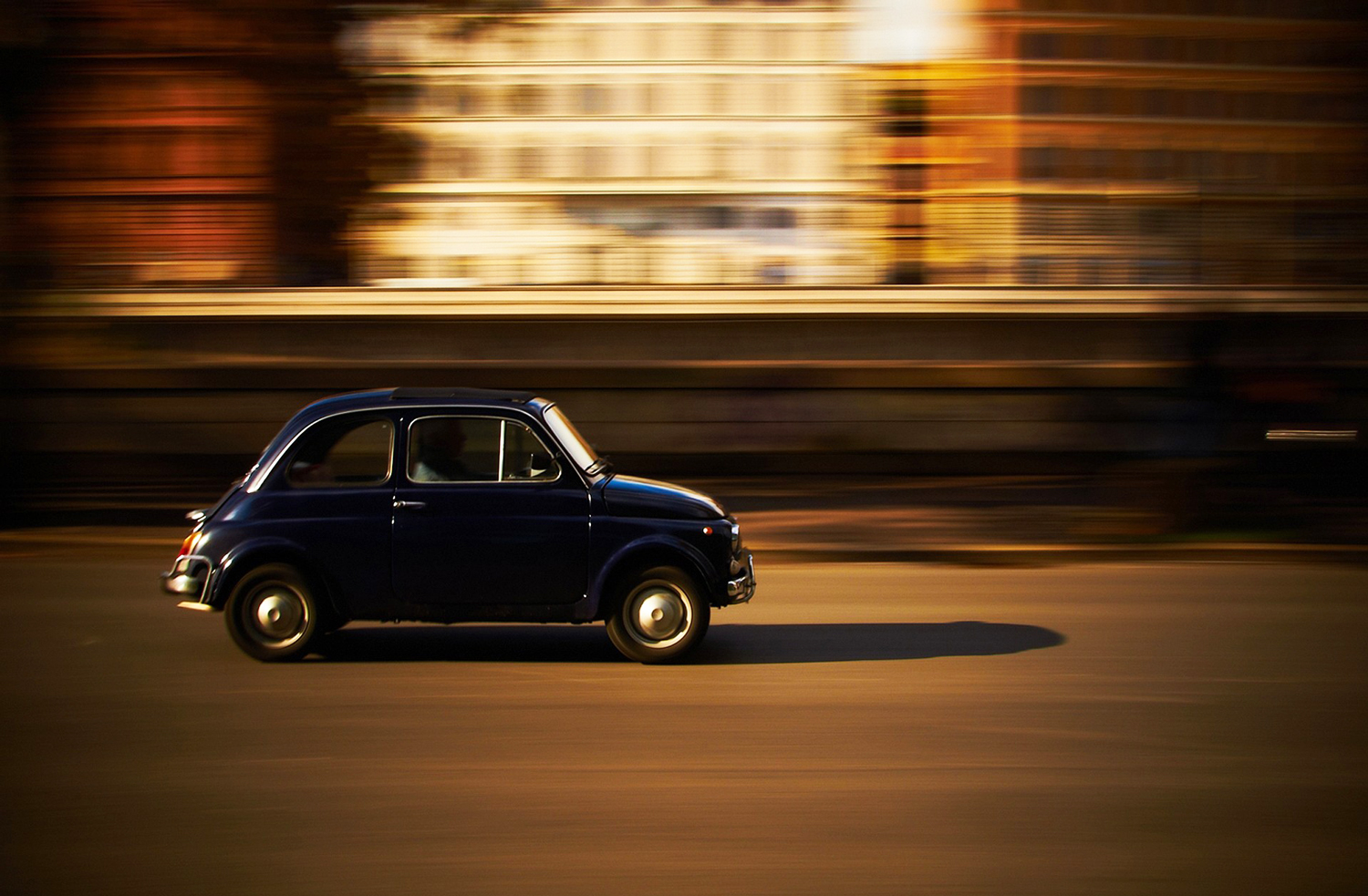 Vintage Fiat 500 driving down a street with motion blur on the background buildings