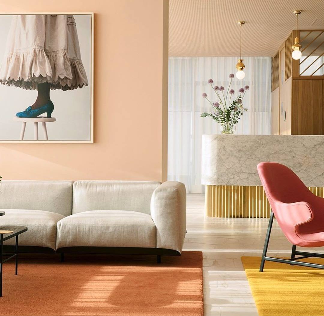 Hotel lobby with a pink sofa, coral armchair and marble reception desk under a framed print