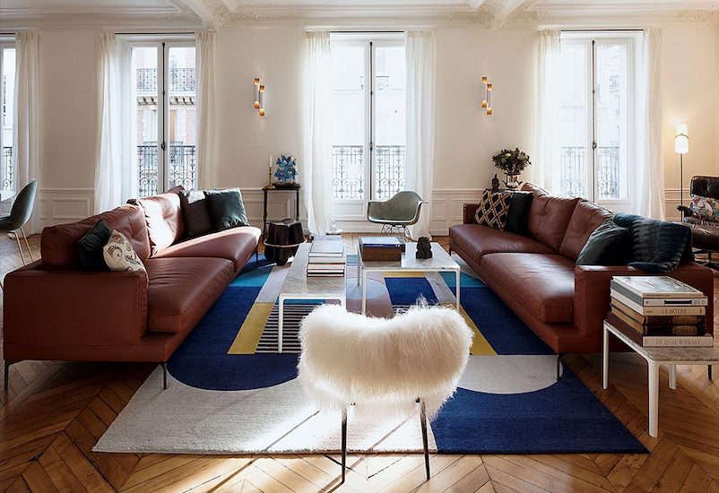 Living room with tall windows, brown leather sofas, a blue patterned rug and herringbone parquet
