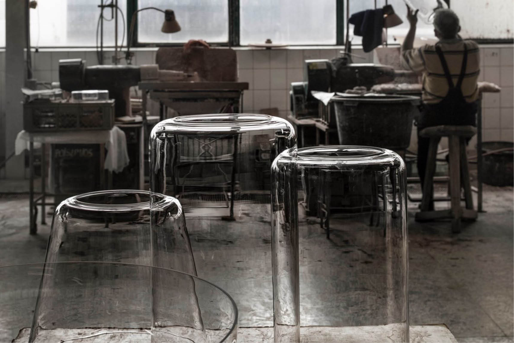 Clear glass stools in a workshop, with an artisan working in the background