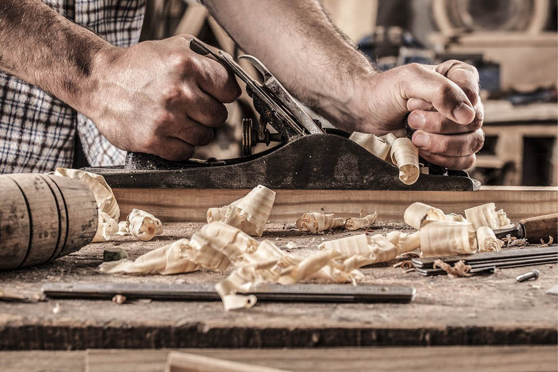 Craftsman planing a wooden board, with wood shavings on the workbench