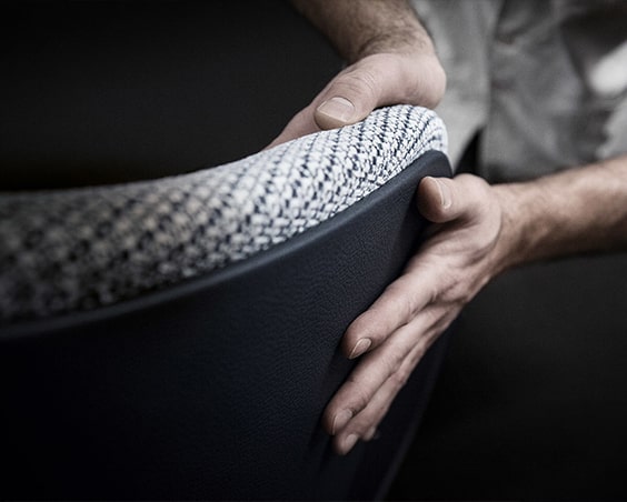 Close-up of two hands adjusting the woven fabric backrest of a dark chair