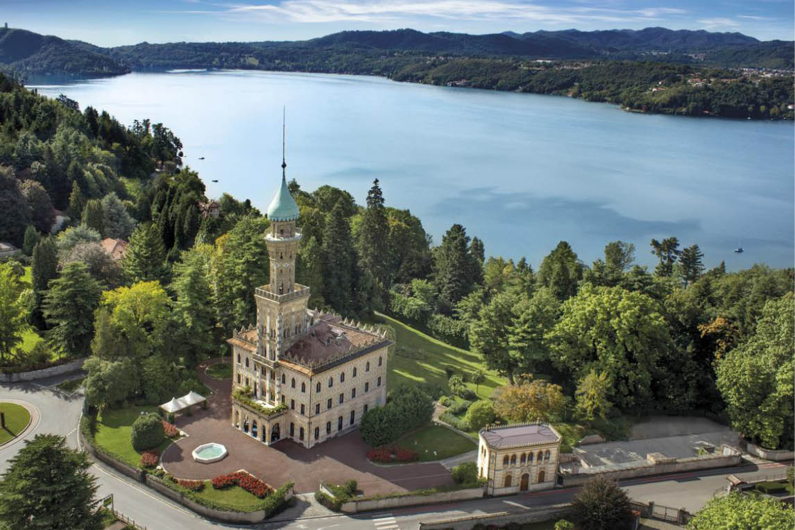Aerial view of a lakeside villa with a tower and turquoise dome surrounded by gardens