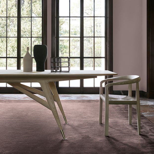 Angular wood dining table and chair by tall paned windows overlooking greenery