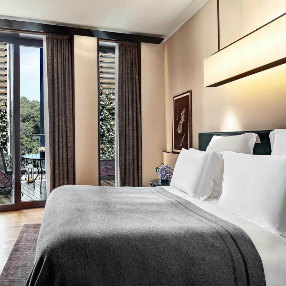 Hotel bedroom with a grey bedspread and a balcony onto trees
