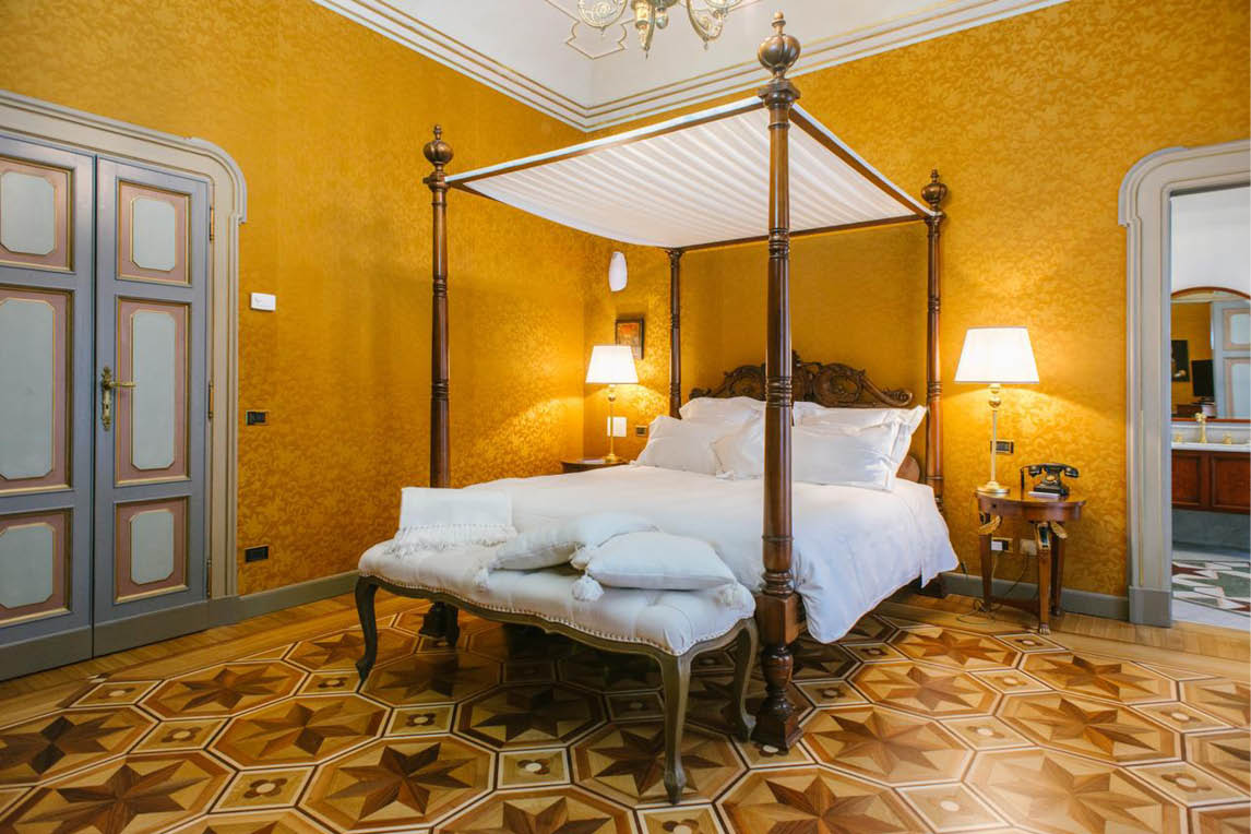 Ornate bedroom with a canopy bed, yellow damask walls and a patterned parquet floor