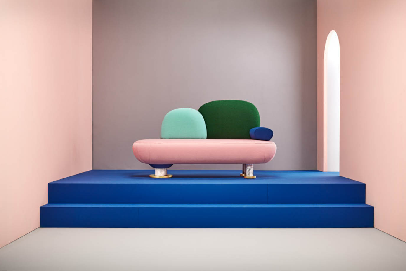 Sculptural pink sofa with green and blue cushions on a blue platform