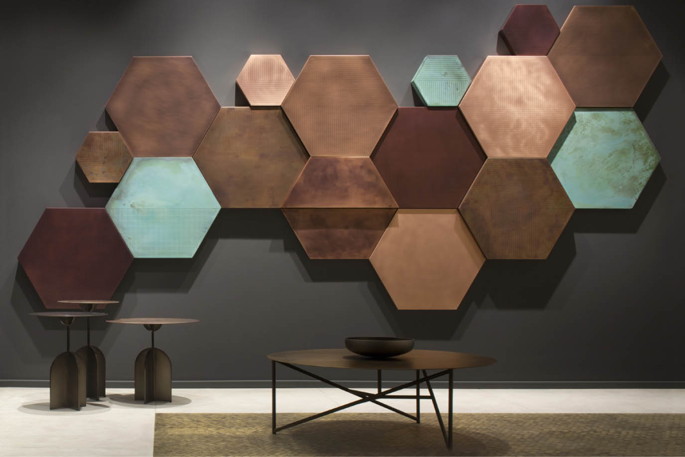 Wall of copper and teal hexagonal panels above low metal tables