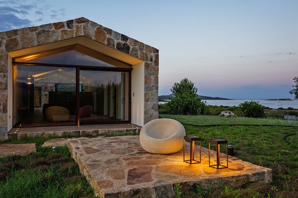 Stone house terrace with glass doors and lounge chair overlooking the sea at dusk
