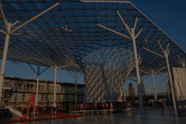 Glass canopy pavilion with tree-like steel supports at a Milan design event