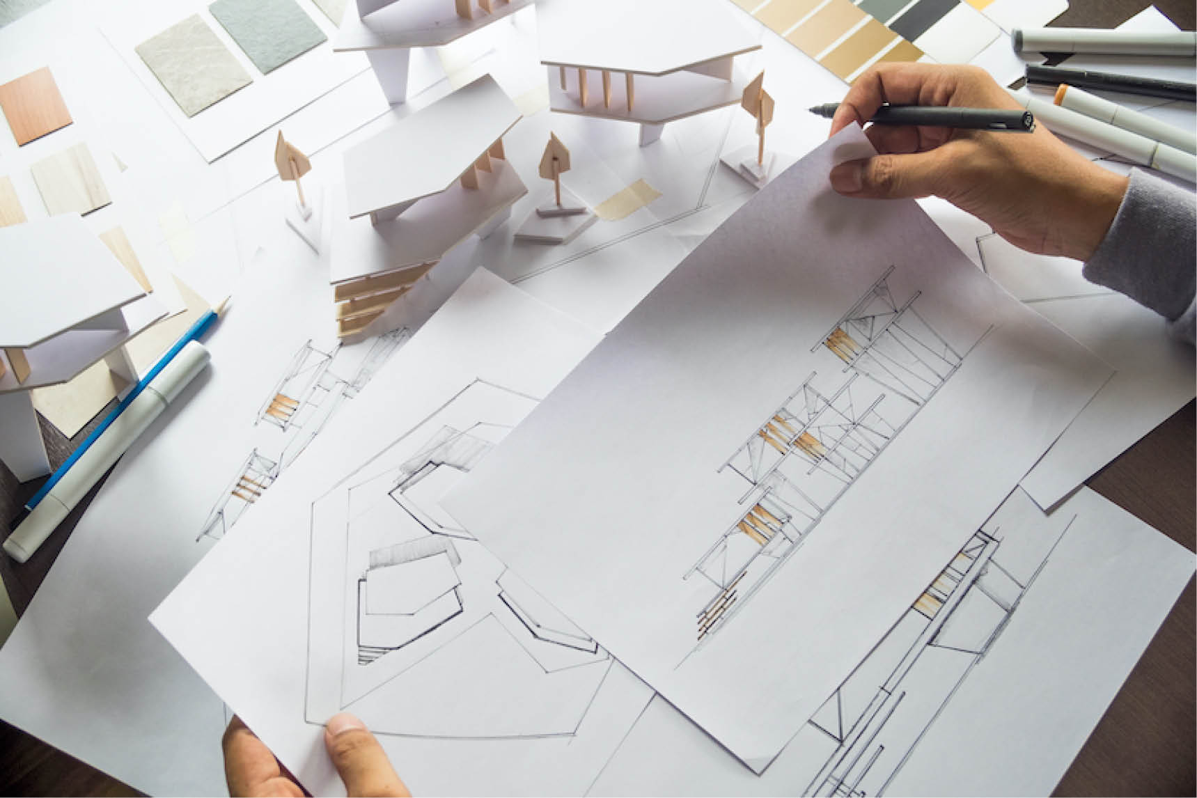 Architect sketching floor plans next to a white architectural model and material samples