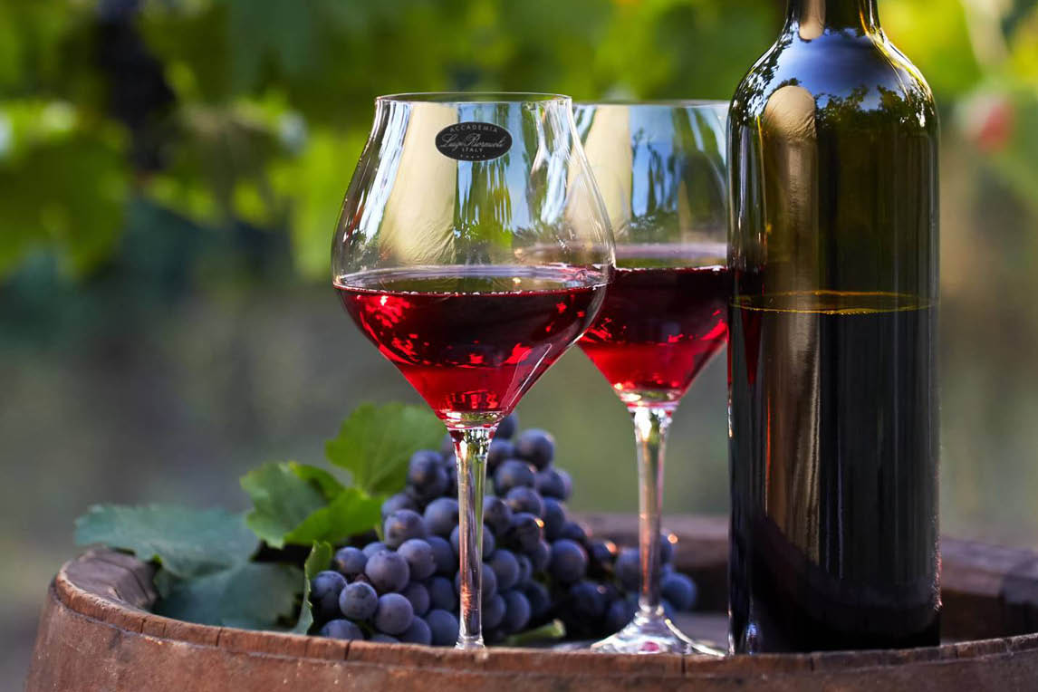 Two glasses of red wine, a bottle and grapes on a barrel