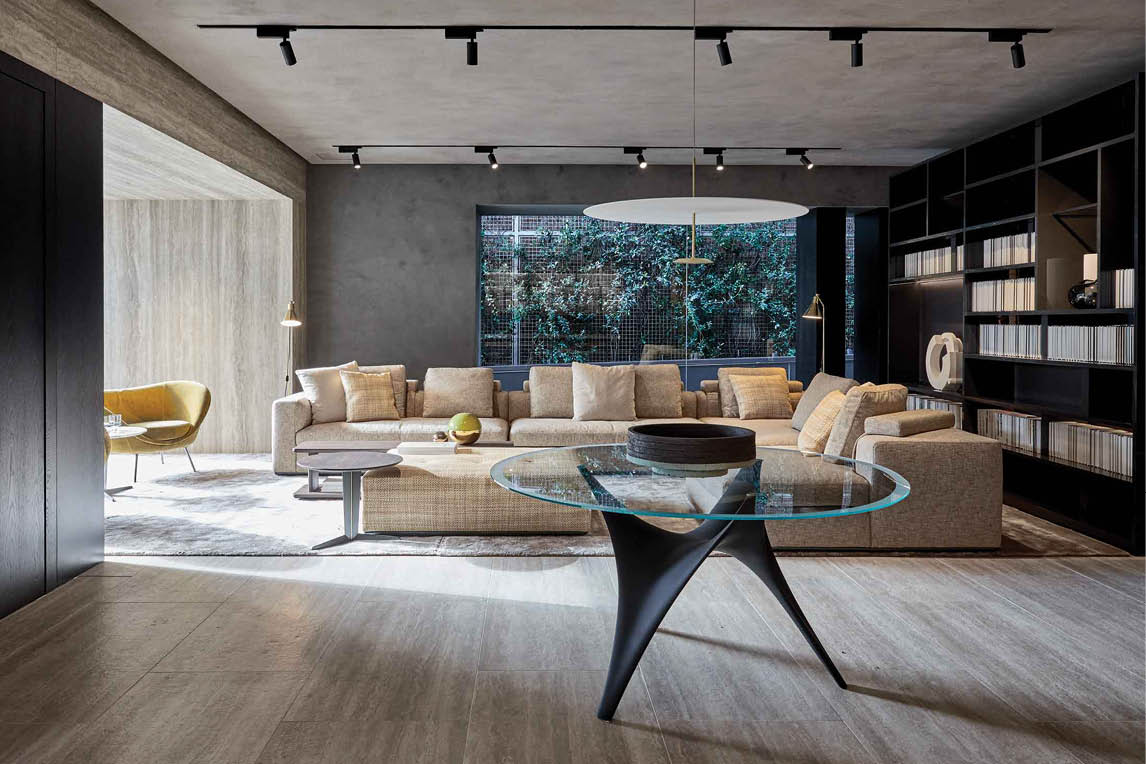 Living room with a beige sofa, glass coffee table, bookshelves and track lighting
