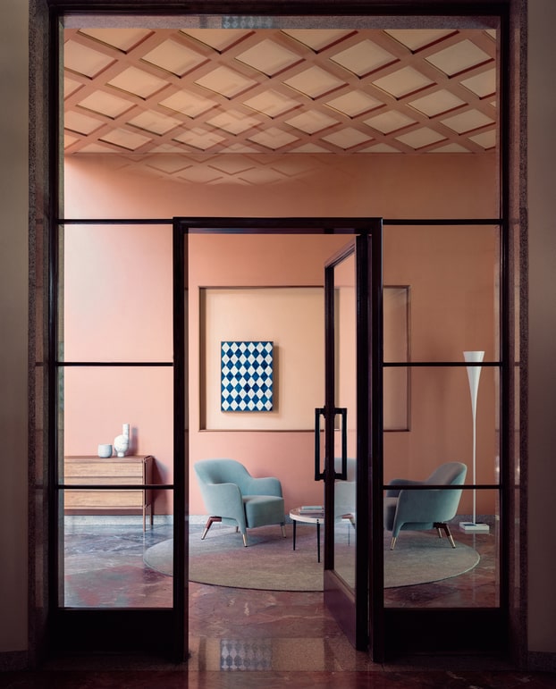 Glass entrance doors opening to a peach-toned room with blue armchairs and artwork