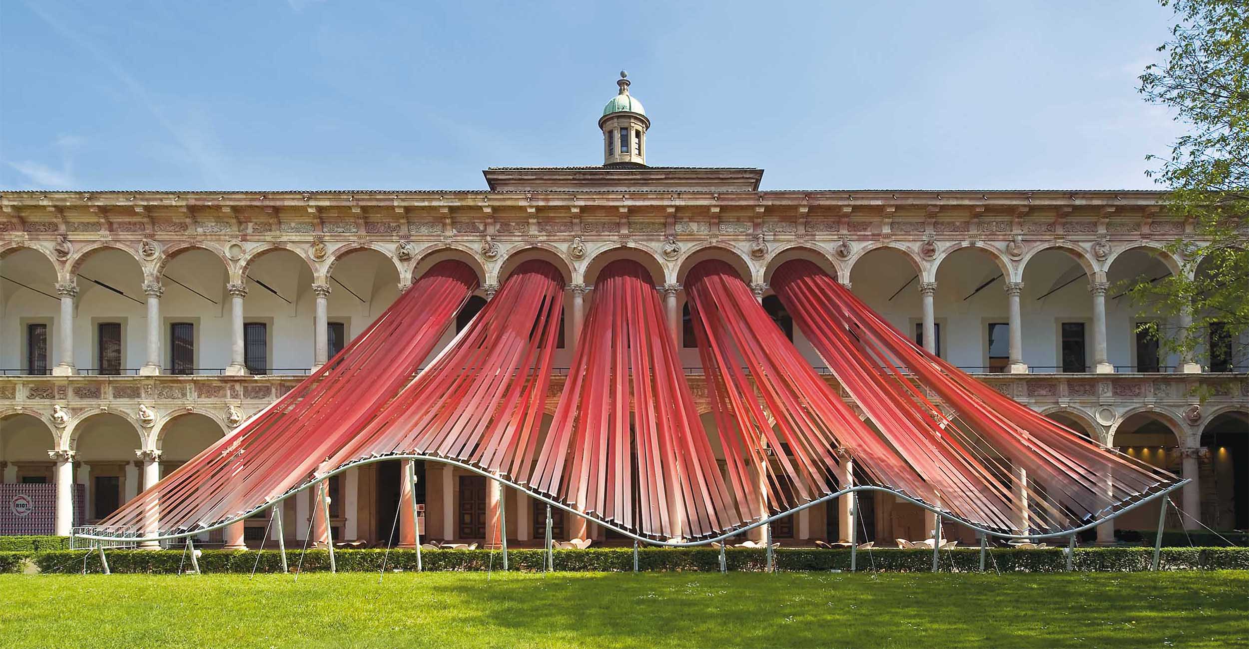 Draped red fabric installation forming a canopy in a historic cloister courtyard