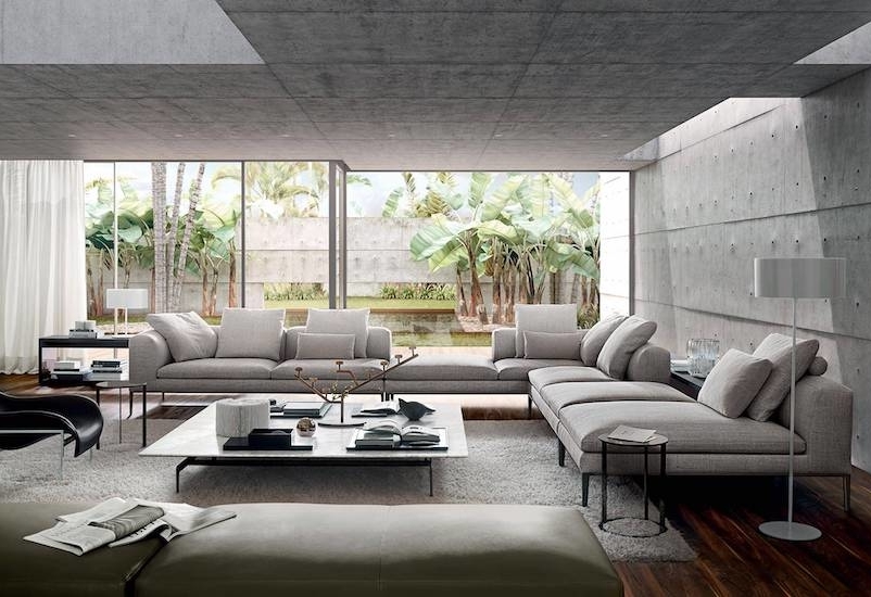 Living room with grey sofas, concrete walls and a glass wall onto a garden