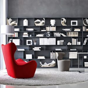Red sculptural armchair and grey chair in front of a dark bookshelf filled with books and decor