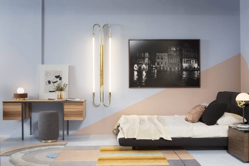 Bedroom with a low black bed, wooden desk, brass wall lamps and a black-and-white night photograph