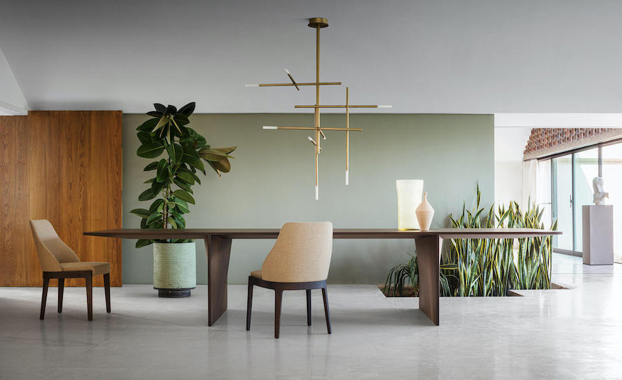 Dining area with a wooden table, beige chair and a linear brass pendant light against a sage green wall