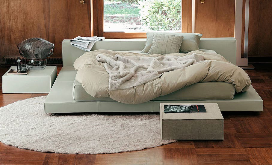 Bedroom with a low sage green upholstered platform bed, rumpled bedding, a shag rug and wood-panelled walls