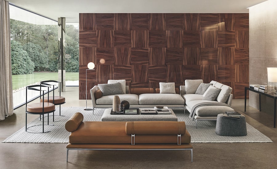 Living room with a light grey sofa, cognac leather bench and a wood parquet-patterned feature wall