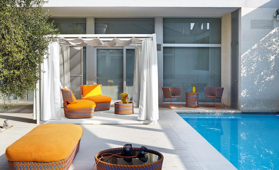 Poolside terrace with orange woven lounge chairs, a white pergola and round rattan side tables