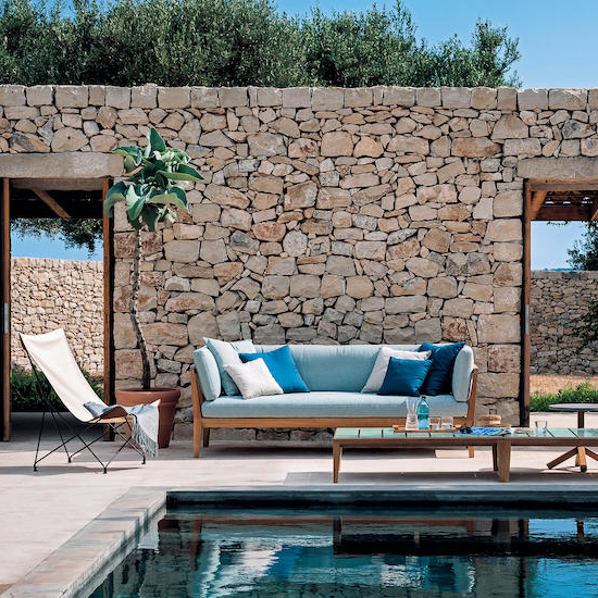 Poolside terrace with a stone wall, teal-cushioned outdoor sofa and folding chair