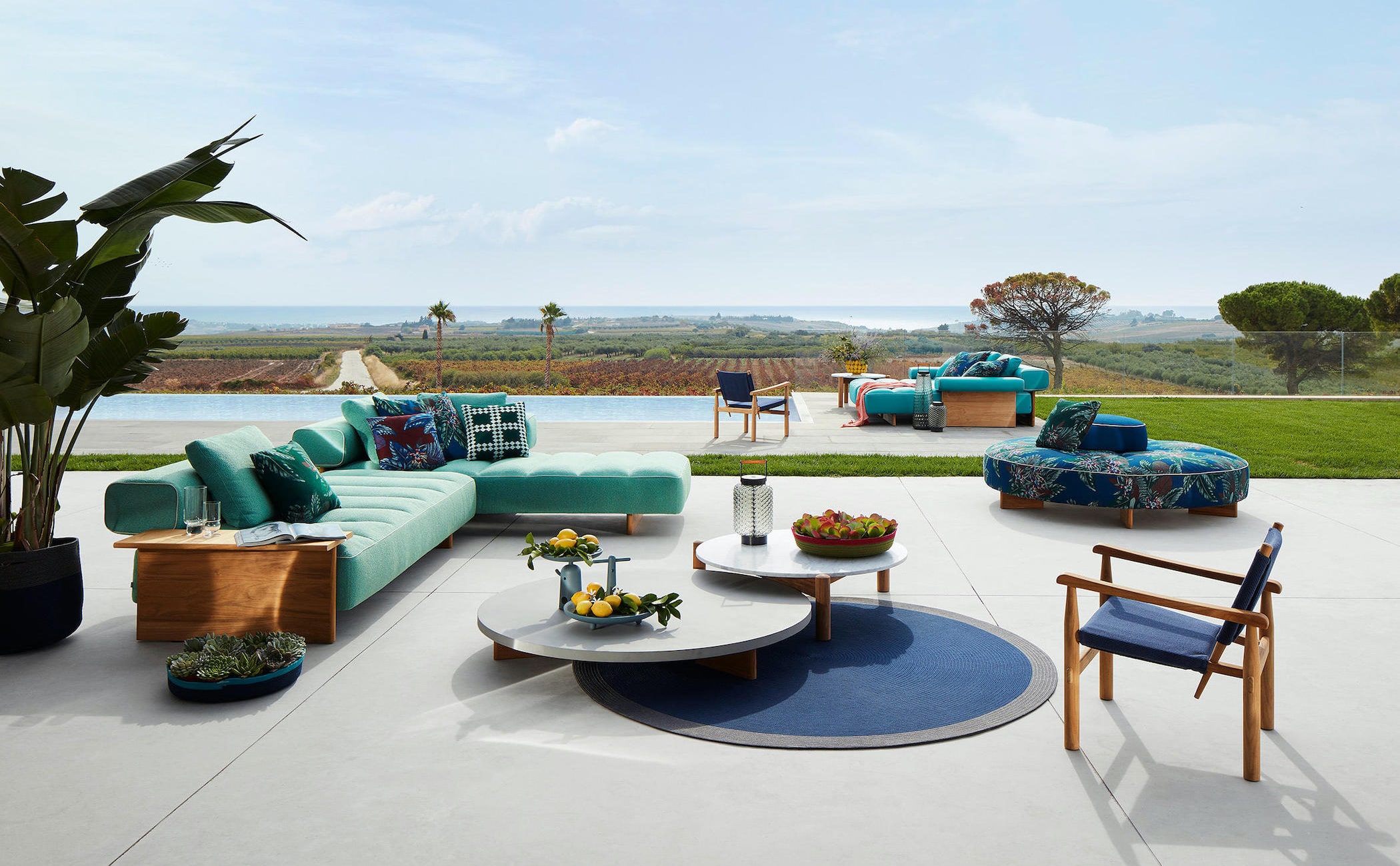 Outdoor lounge with a teal modular sofa, round nesting tables and a pool overlooking vineyards